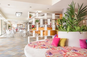 A modern hotel lobby with a seating area featuring colorful patterned cushions, a reception desk, and various potted plants. - Flisvos Royal Tolo (Nafplio)
