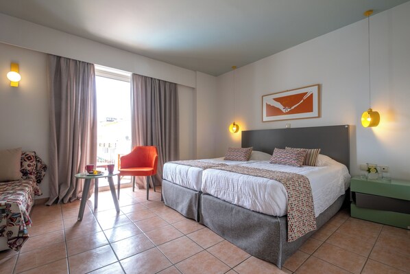 A hotel room with a bed, a chair, a small table, and a window with curtains. - Flisvos Royal Tolo (Nafplio)