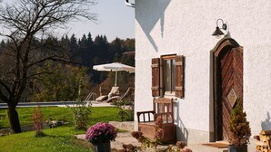 A house with a wooden door, a small porch with a chair, and a garden with flowers and a tree. - "Melkerhaus" bis 6 Personen mit Terrasse und Pool, 101m² (Wonneberg)