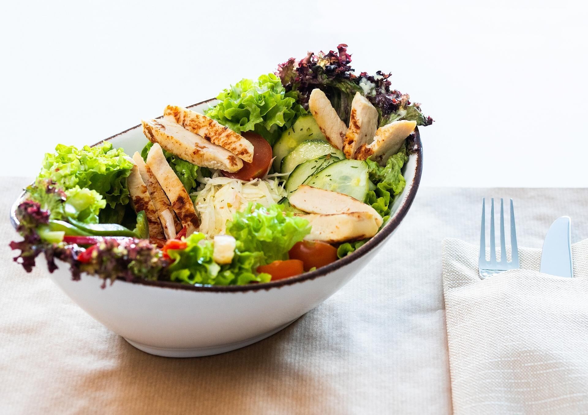 Un saladier de salade composée avec du poulet grillé, des concombres, des tomates et un mélange de jeunes pousses.