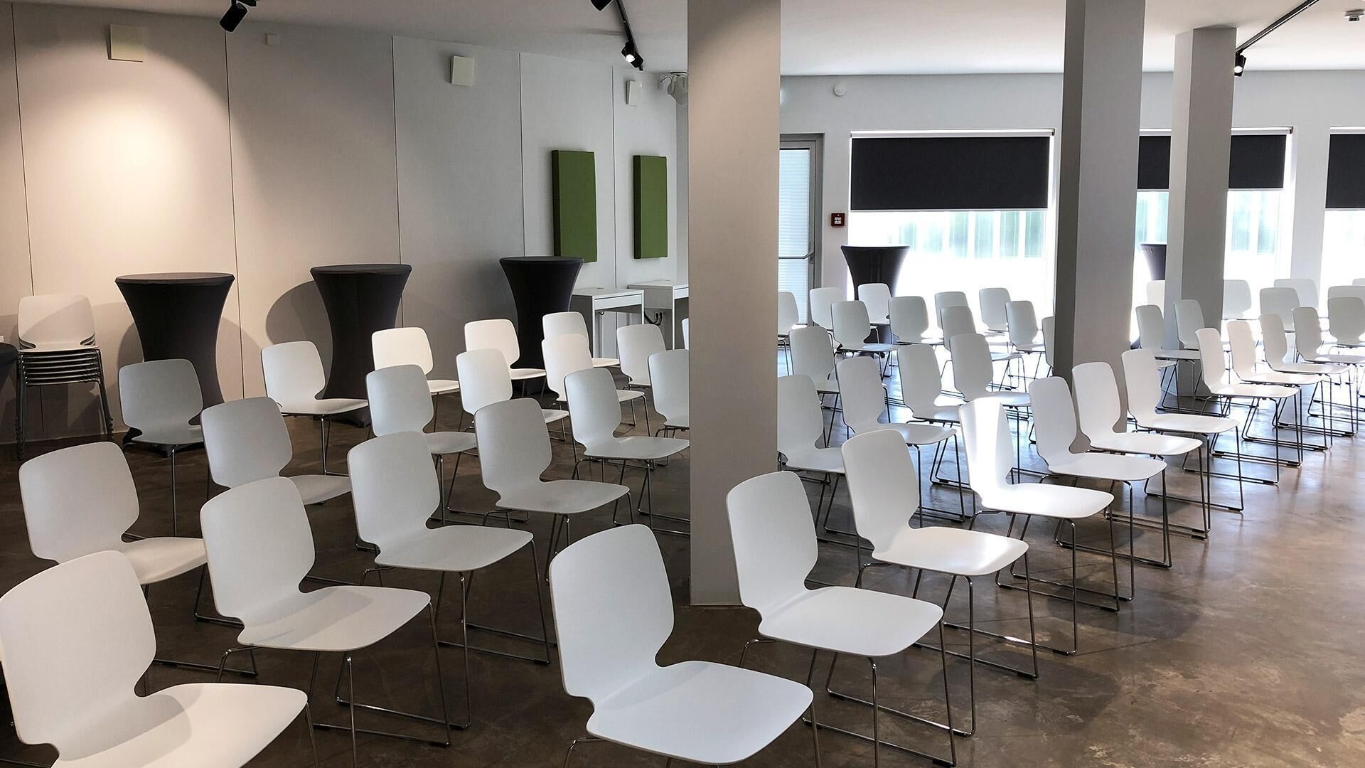 A spacious room with rows of white chairs and tables, large windows, and a modern design.