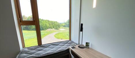 A room with a bed, a desk, and a window overlooking a green landscape.
