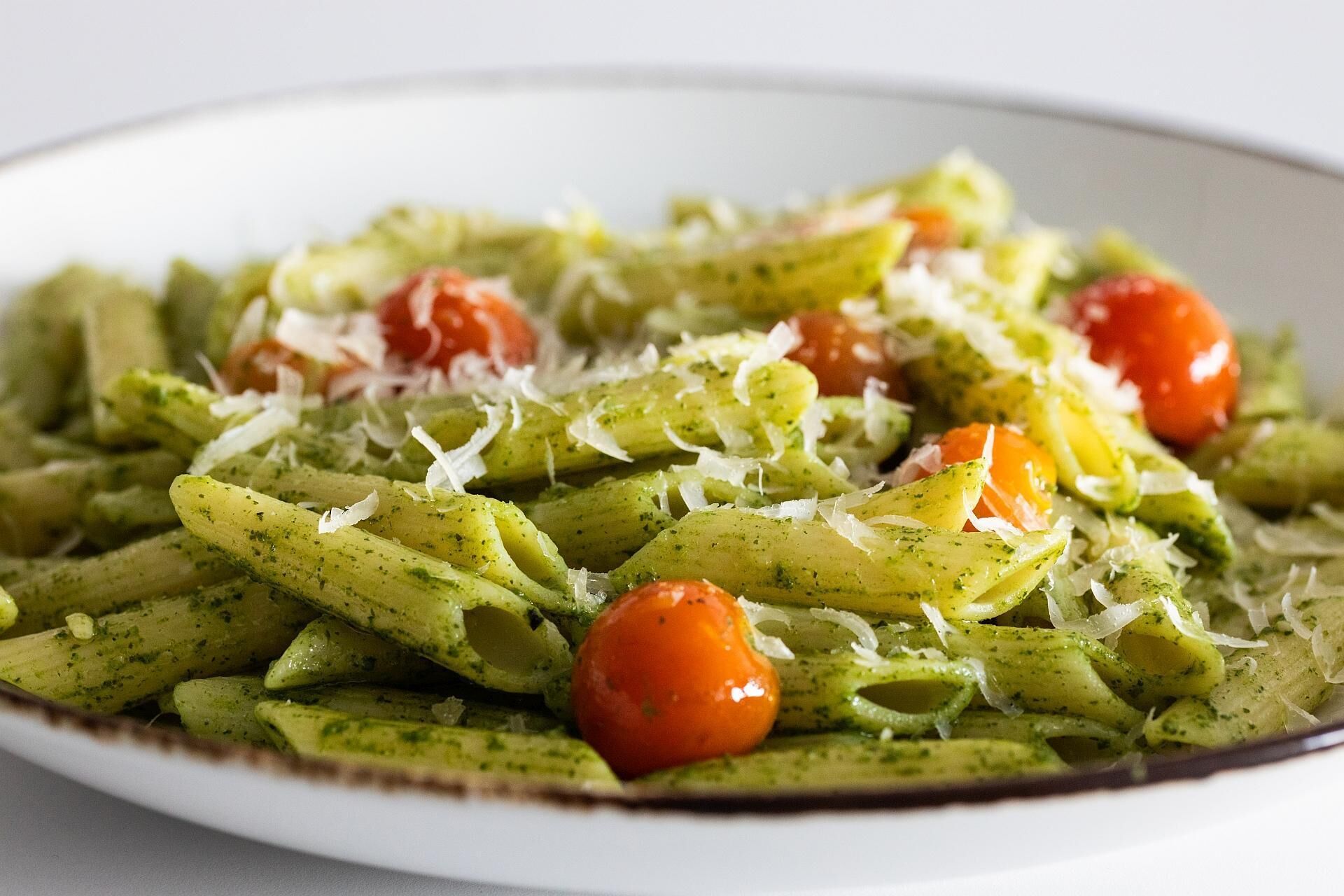 A plate of pasta with green sauce, cherry tomatoes, and grated cheese.