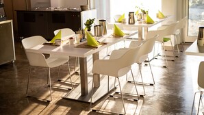 Un comedor moderno con sillas y mesas blancas, una cocina al fondo y vistas por la ventana.
