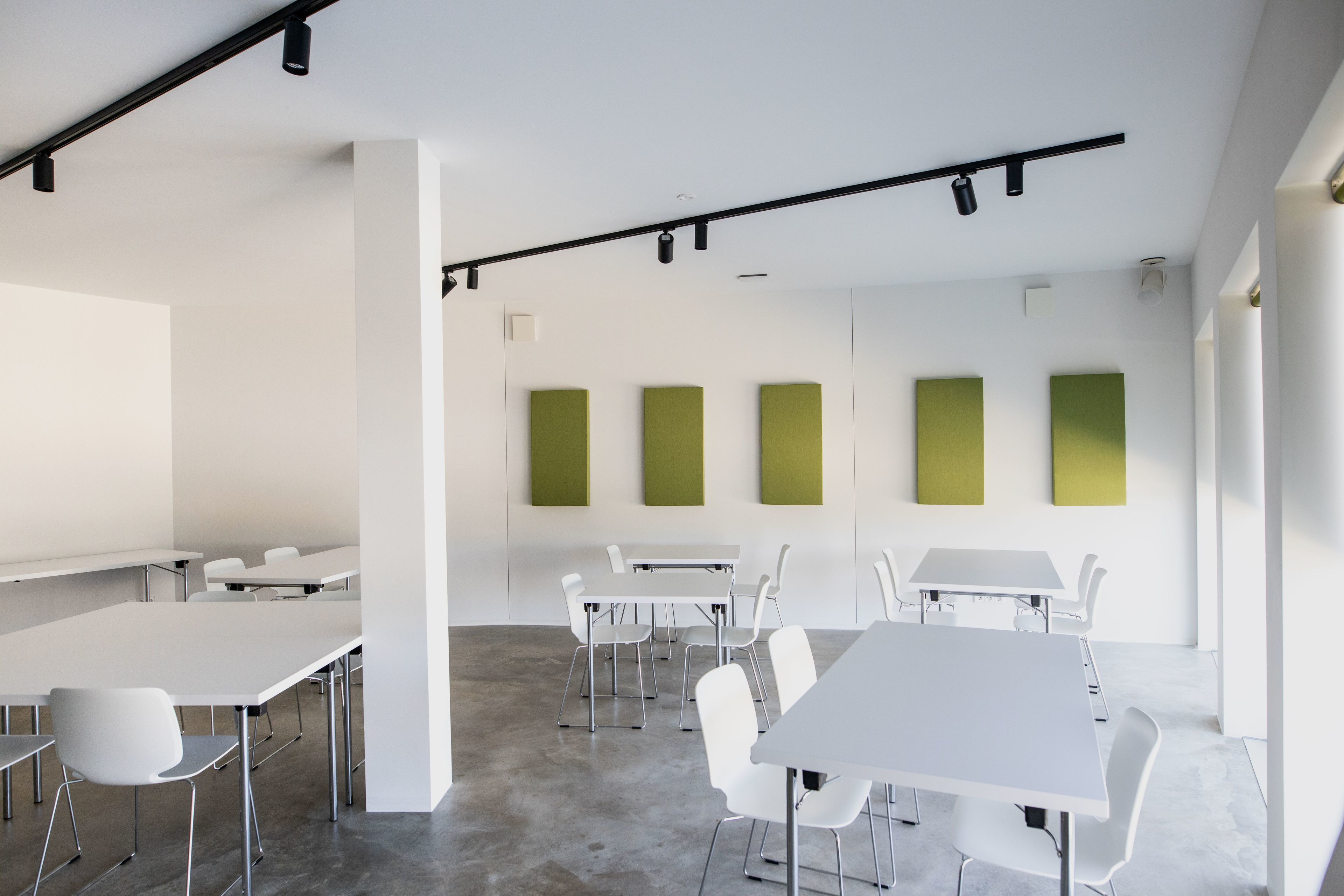 Una sala de conferencias moderna con mesas y sillas blancas, suelo gris y paneles verdes decorativos en las paredes.