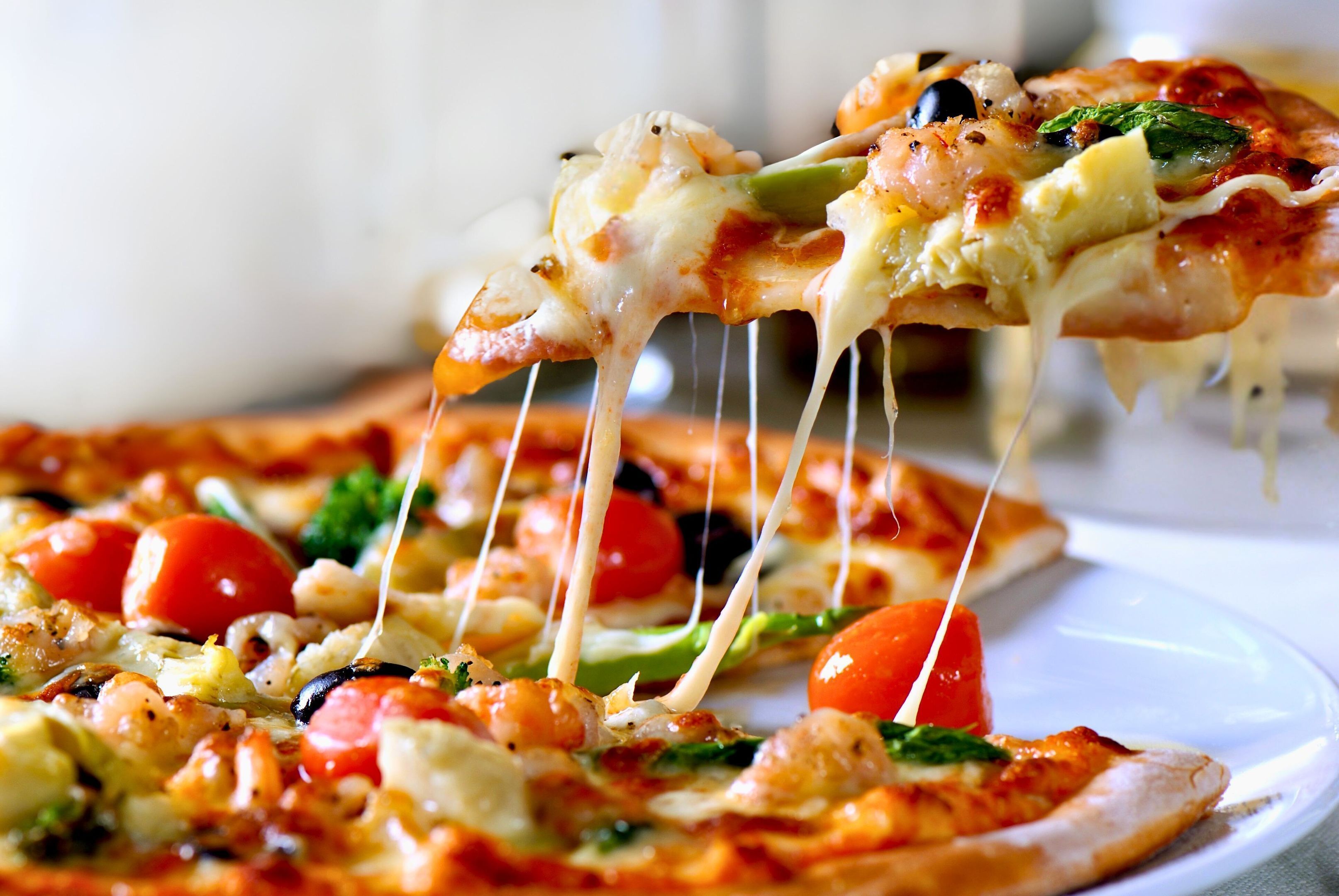 Lähikuva pizzasta, jossa näkyvät selvästi päällä olevat ainekset, kuten tomaatit, oliivit ja juusto.