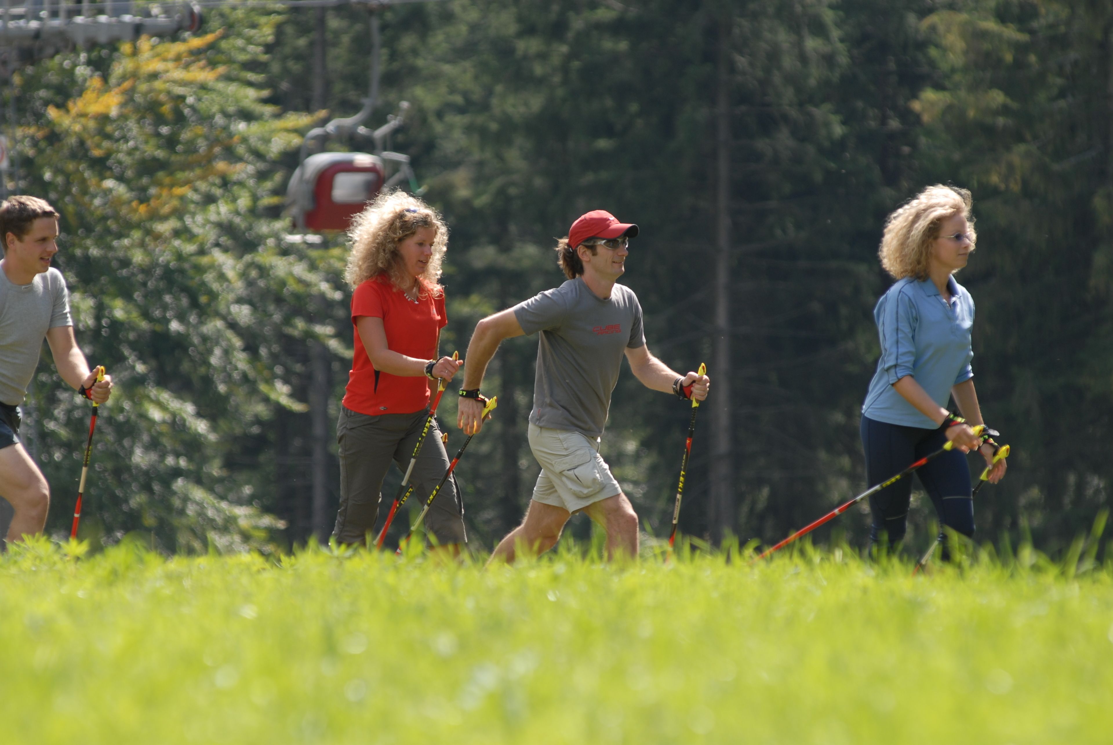 A group of people hiking in a grassy area with trees and a ski lift in the background.