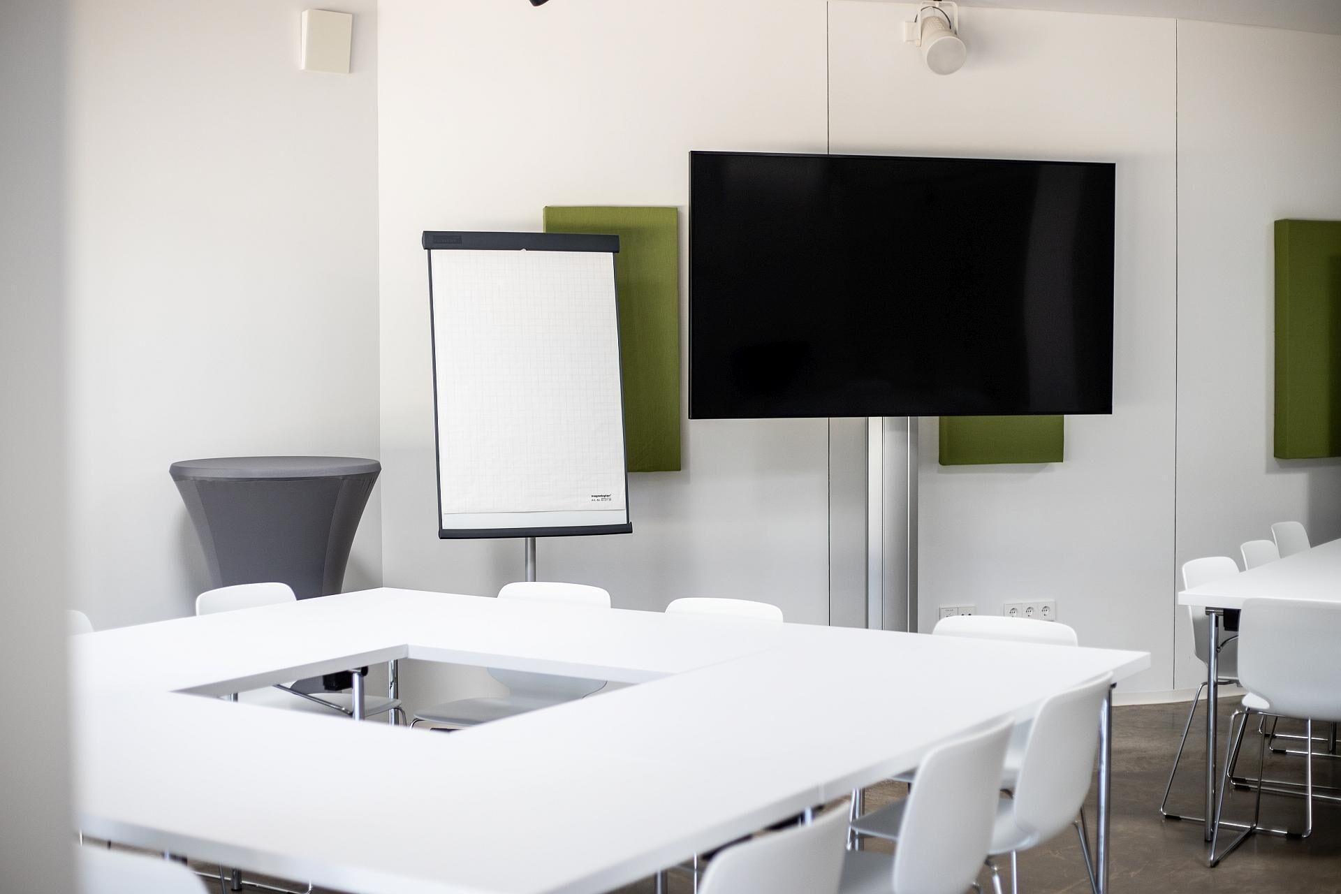Une salle de conférence avec des tables blanches, un grand téléviseur à écran plat et un tableau blanc.