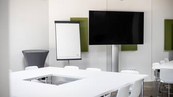 Une salle de conférence avec des tables blanches, un grand téléviseur à écran plat et un tableau blanc.