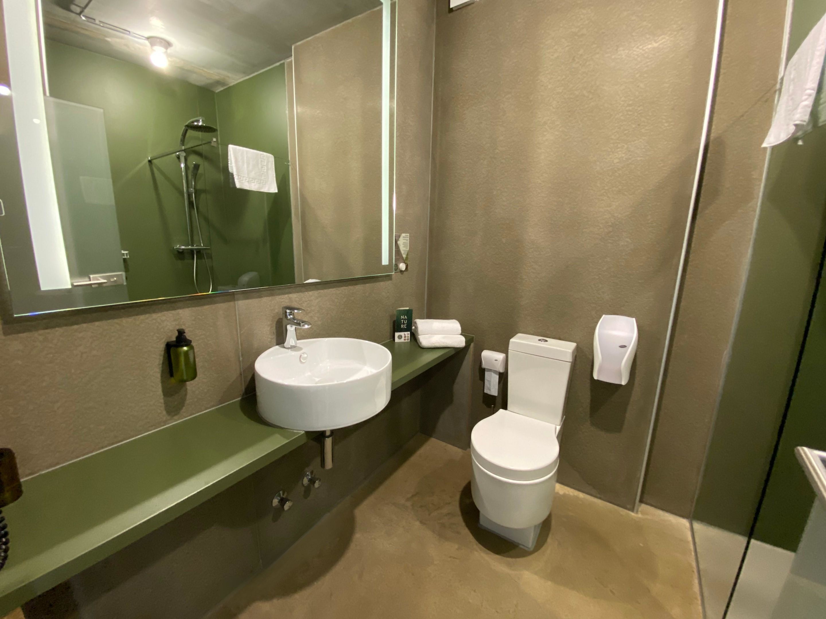 A modern bathroom with a large mirror, a sink, a toilet, and a shower.