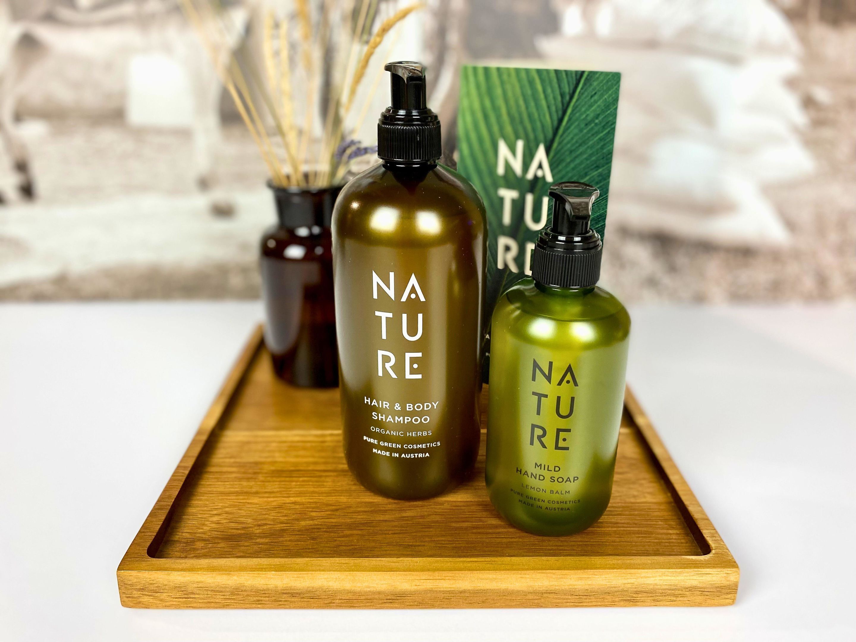 Three bottles of Nature brand hair and body shampoo, a bottle of Nature hand soap, and a Nature product box on a wooden tray.
