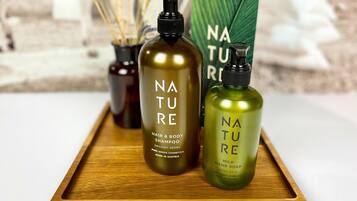 Three bottles of Nature brand hair and body shampoo, a bottle of Nature hand soap, and a Nature product box on a wooden tray.