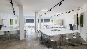 Una sala de conferencias moderna con una gran mesa blanca, varias sillas blancas y una pizarra.