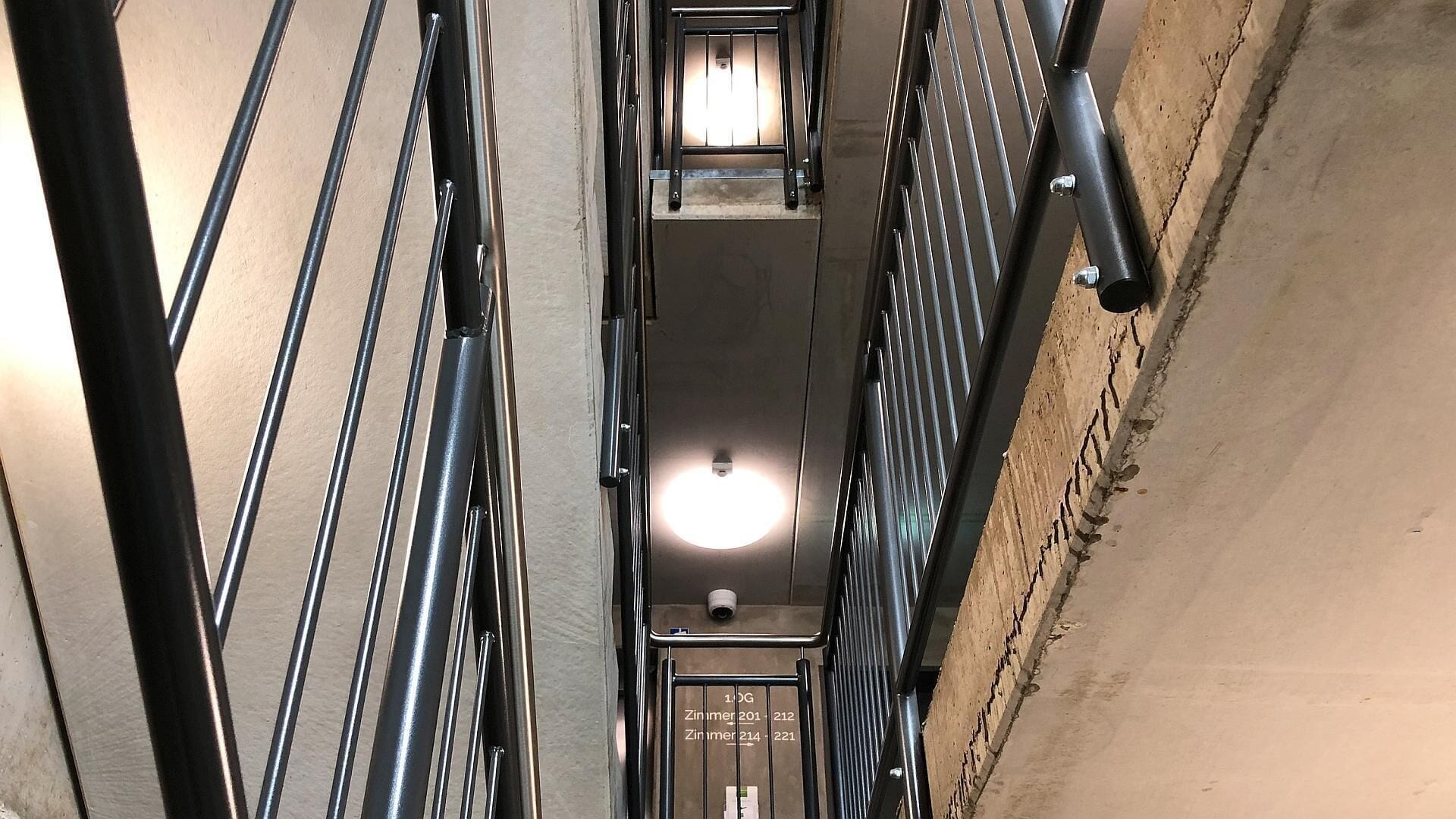 Un hueco de ascensor estrecho, con estructura metálica y un accesorio de iluminación en la parte superior.