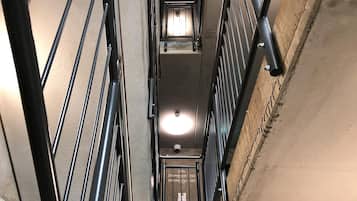 Un hueco de ascensor estrecho, con estructura metálica y un accesorio de iluminación en la parte superior.