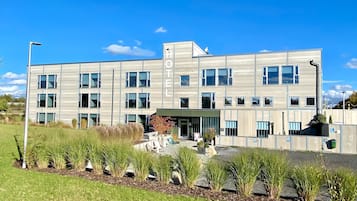 A modern hotel with a flat roof, multiple windows, and a landscaped front yard.