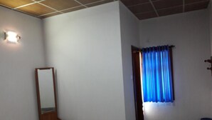 A room with a wooden desk, a mirror, a small table, a blue curtain, and a light fixture on the wall. - Ulpatha Nature Resort (Kobeigane)