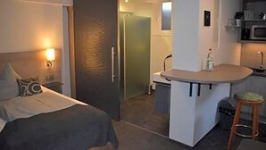 A hotel room with a bed, a small kitchenette, and a bathroom.