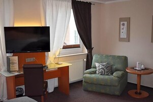 Una habitación con televisión, escritorio, silla, sofá y una pequeña mesa con tetera.