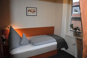 A single bed with a wooden headboard, a bedside lamp, and a framed picture on the wall.