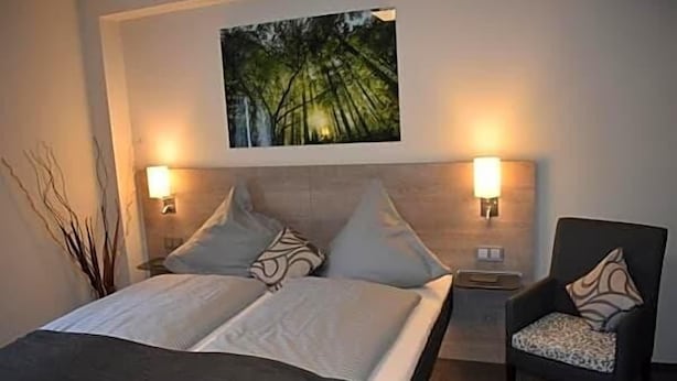 A hotel room with a bed, two bedside lamps, a chair, and a painting on the wall.