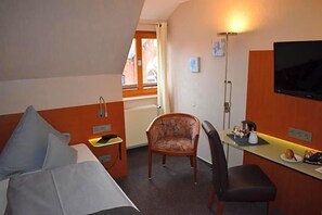 A hotel room with a bed, a desk, a chair, a TV, and a window.