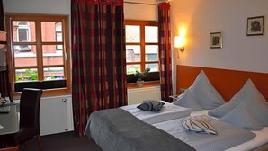 A hotel room with a bed, a desk, a chair, and a window with curtains.