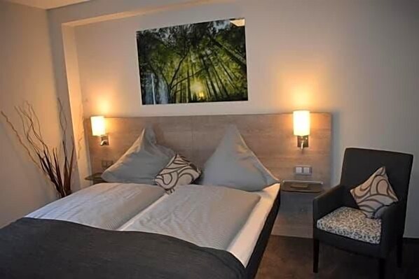 A hotel room with a bed, two bedside lamps, a chair, and a painting on the wall.