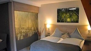 A modern bedroom with a bed, two bedside lamps, a large window, and a painting on the wall.