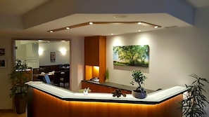 Un mostrador de recepción con acabado de madera y una planta integrada. Encima del mostrador, en la pared, hay un cuadro con un árbol.