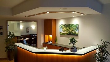 A reception desk with a wooden finish and a built-in plant. There is a framed picture of a tree on the wall above the desk.