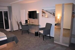 A hotel room with a bed, a desk, a chair, a TV, and a wardrobe.