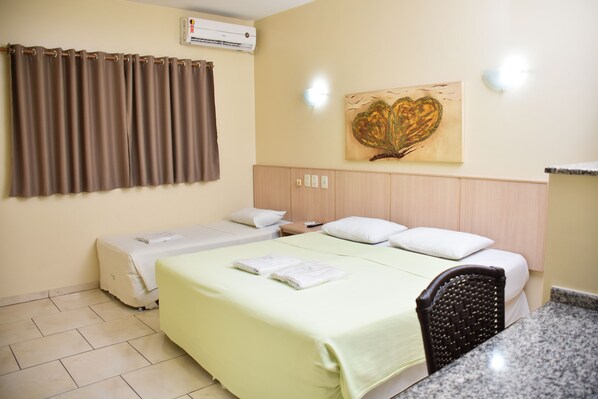 Ein Hotelzimmer mit Bett, Sessel, Tisch, einer Wand-Klimaanlage und einem Gemälde.