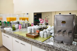 Ein Frühstücksbuffet mit verschiedenen Getränkespendern, einer Kaffeemaschine und einer Auswahl an Tassen und Behältern.