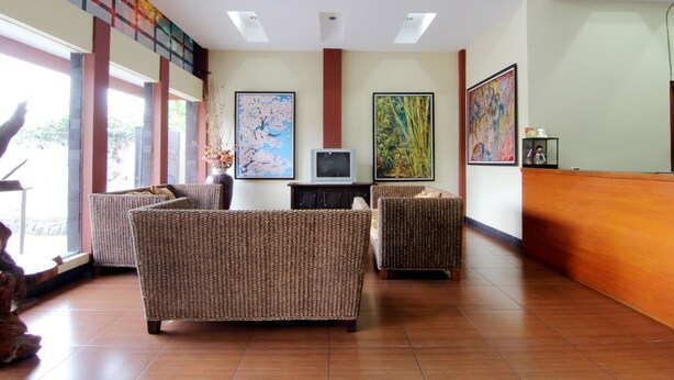 A lobby with wicker furniture, a television, and artwork on the walls. - Hotel Tiger Yogyakarta (Depok)