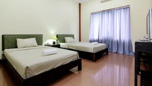 A hotel room with two single beds, a desk, a chair, a lamp, and a window with curtains. - Hotel Tiger Yogyakarta (Depok)