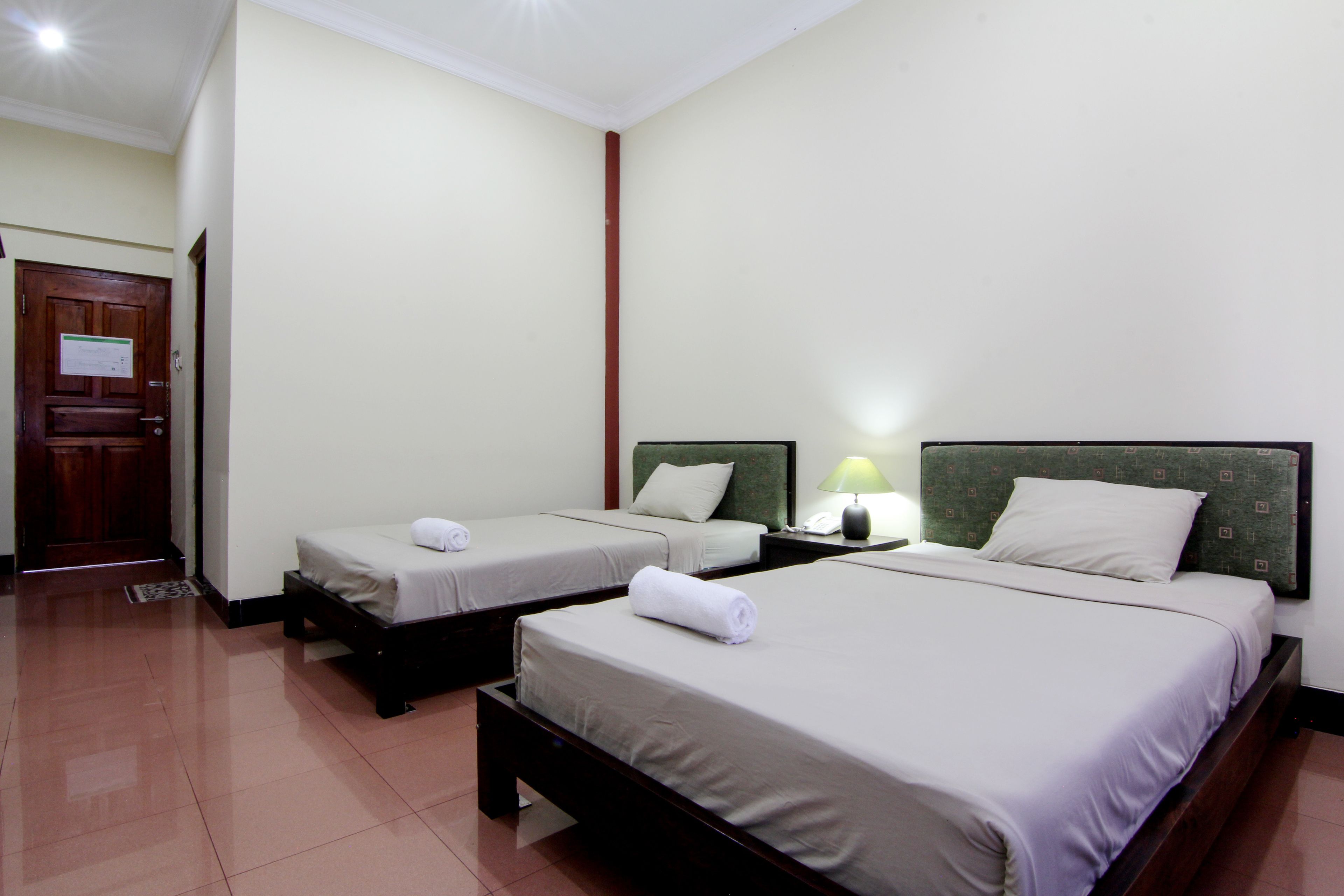 A hotel room with two single beds, a wooden door, and a nightstand with a lamp.