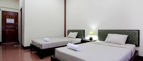 A hotel room with two single beds, a wooden door, and a nightstand with a lamp.