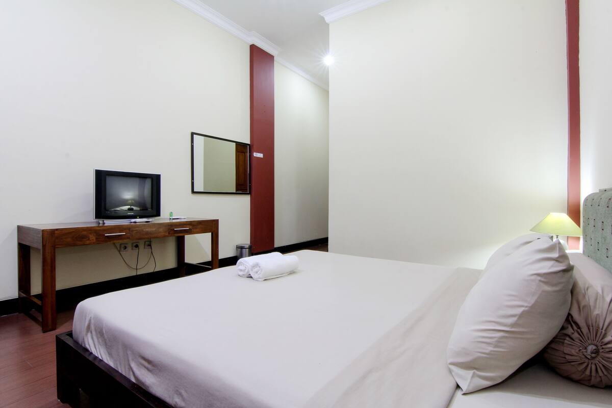 Une chambre d’hôtel avec un lit, un bureau en bois, une télévision, un miroir et une lampe.