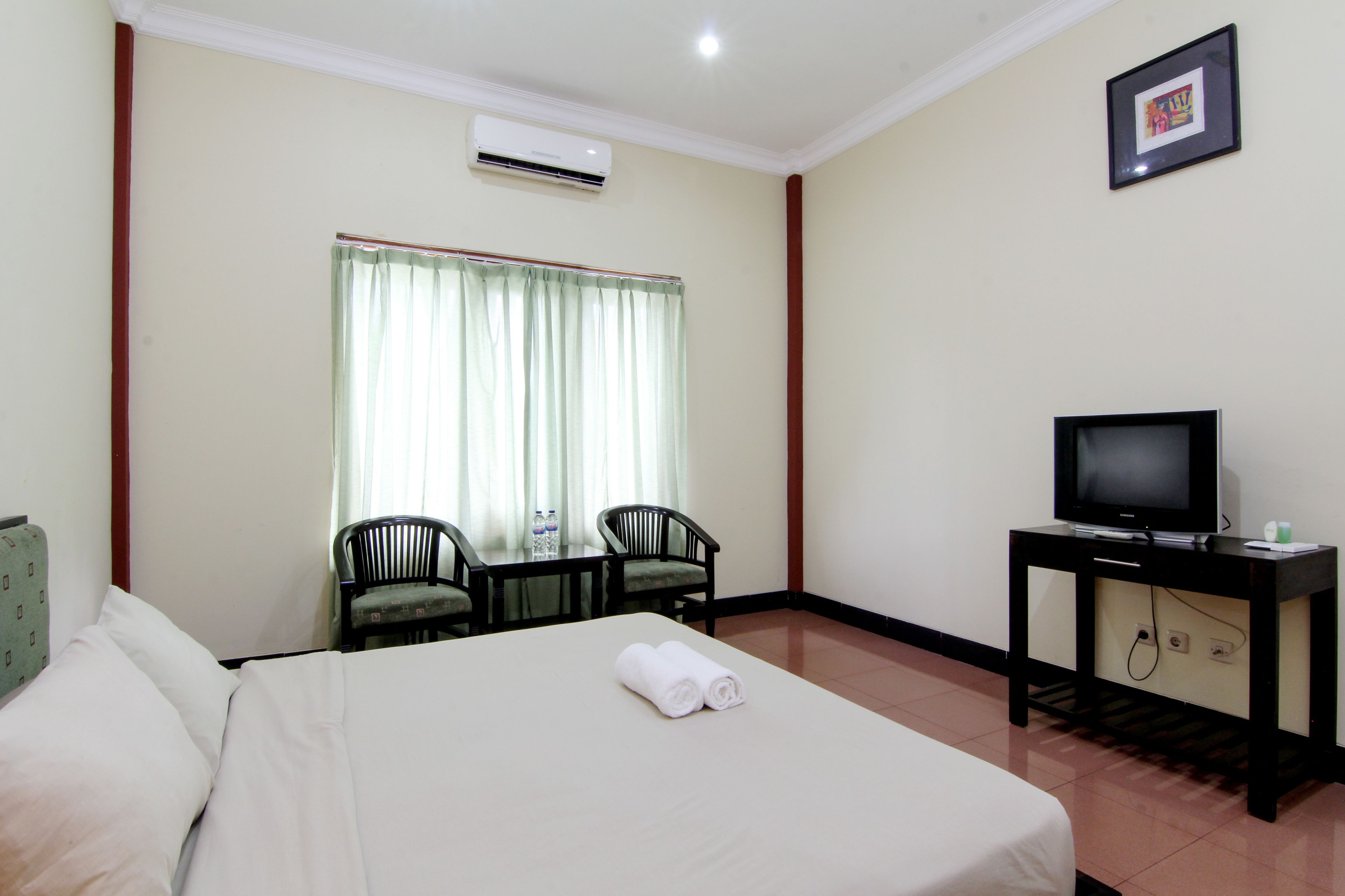 A hotel room with a bed, a television on a stand, a table with chairs, and a window with curtains.