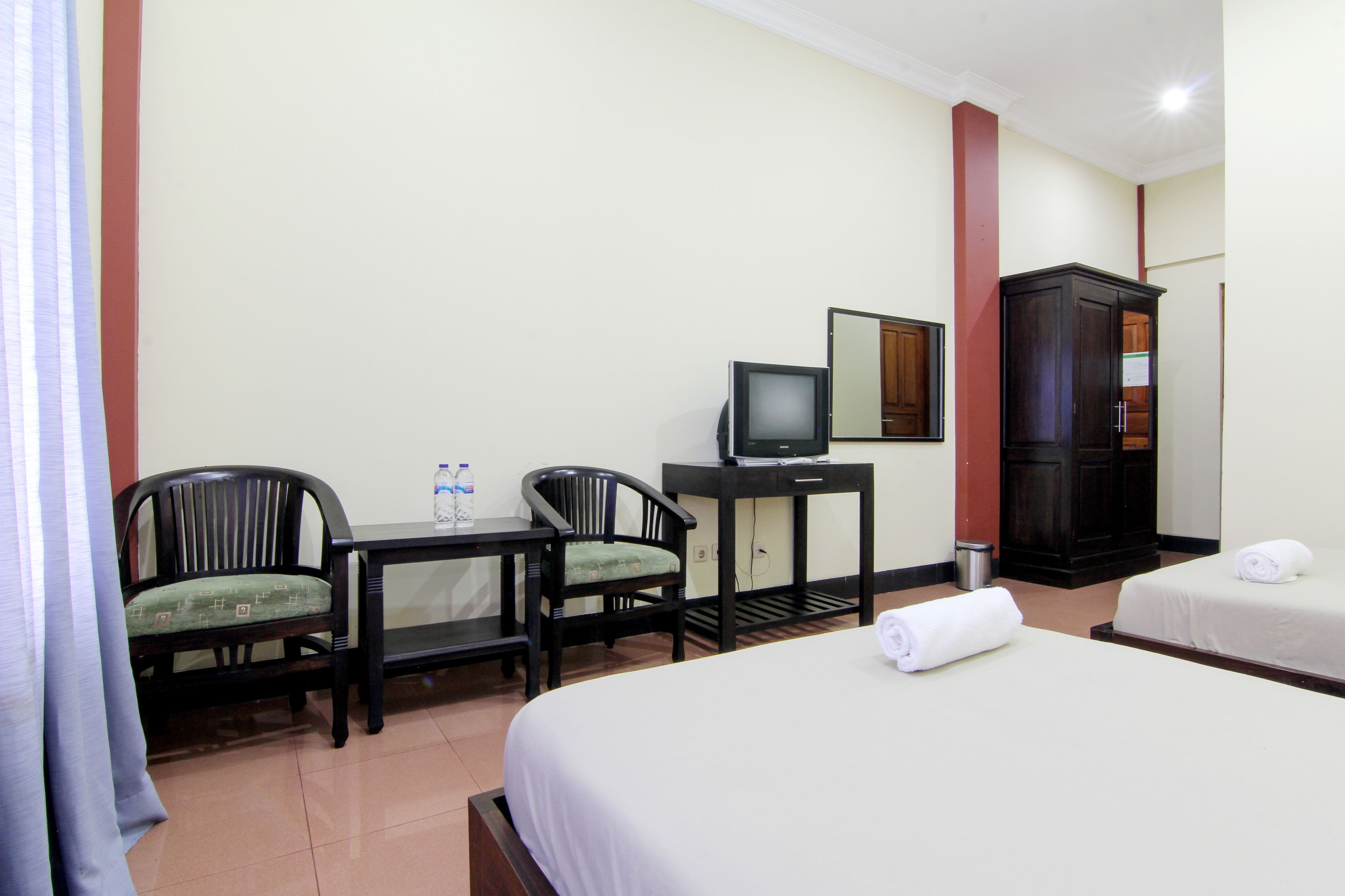 Una habitación de hotel con dos camas individuales, un escritorio con silla, un televisor y un armario.