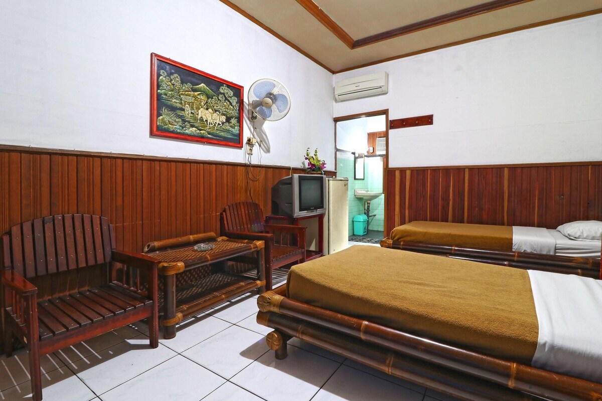 A room with a bed, a wooden chair, a television, and a fan.