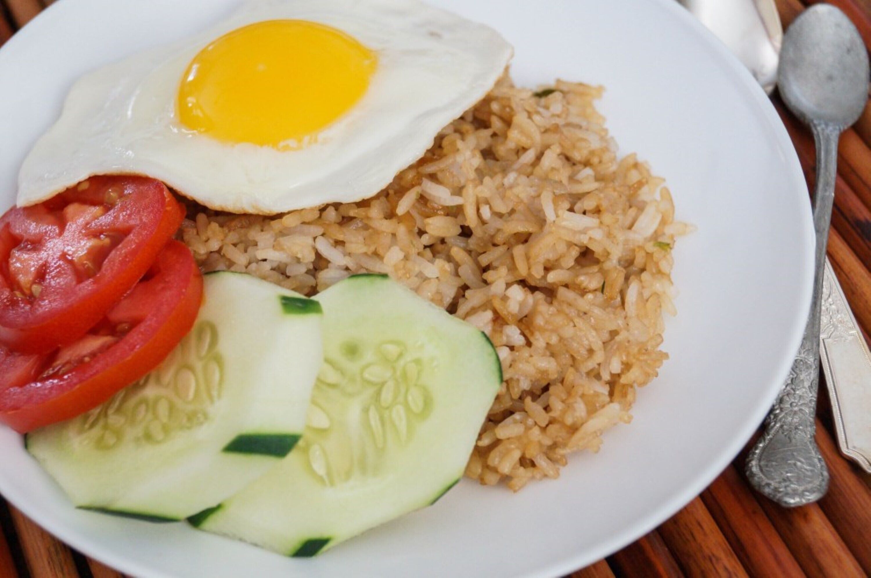 Un plato de arroz frito, un huevo frito, rodajas de tomate y rodajas de pepino.