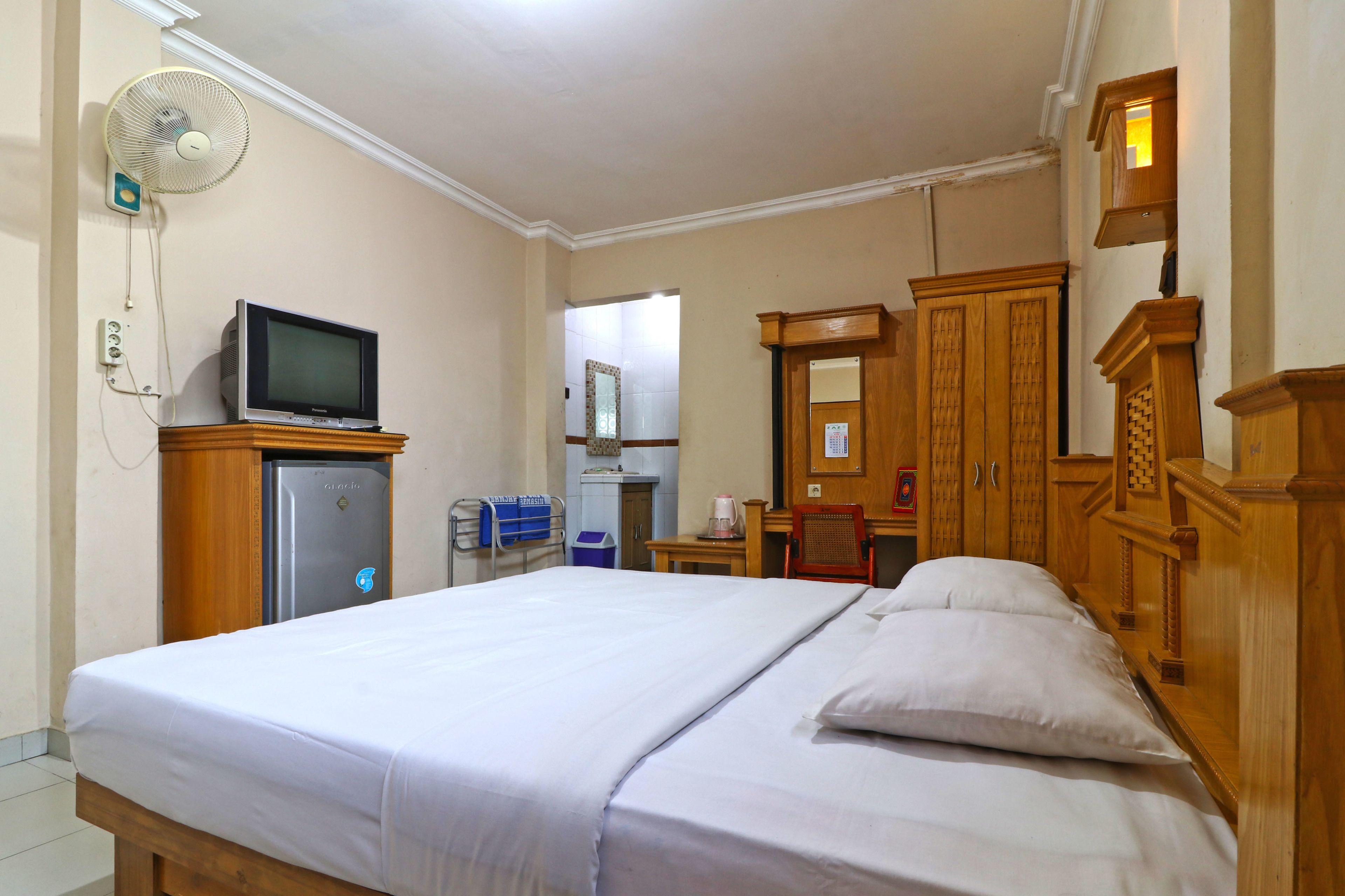 Une chambre d’hôtel équipée d’un lit, d’une télévision, d’un réfrigérateur, d’un miroir et de meubles en bois.