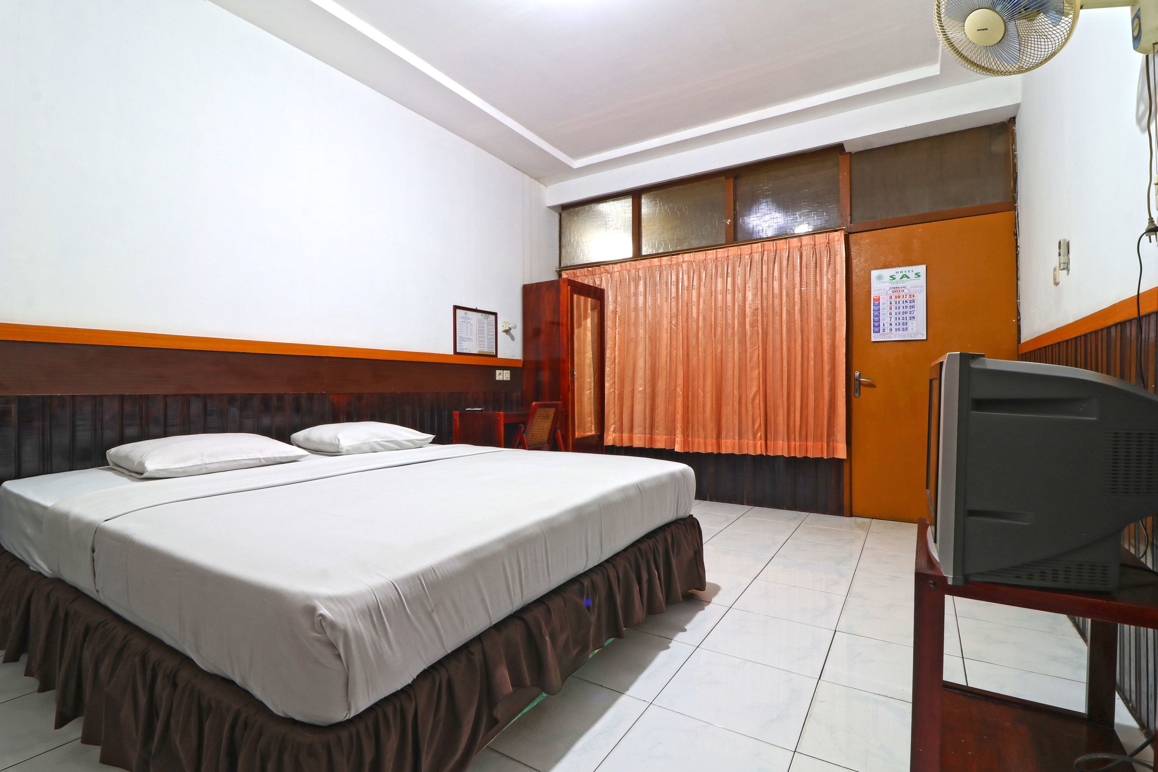 Quarto de hotel com uma cama, uma televisão, um calendário na parede e uma porta com cortinas.