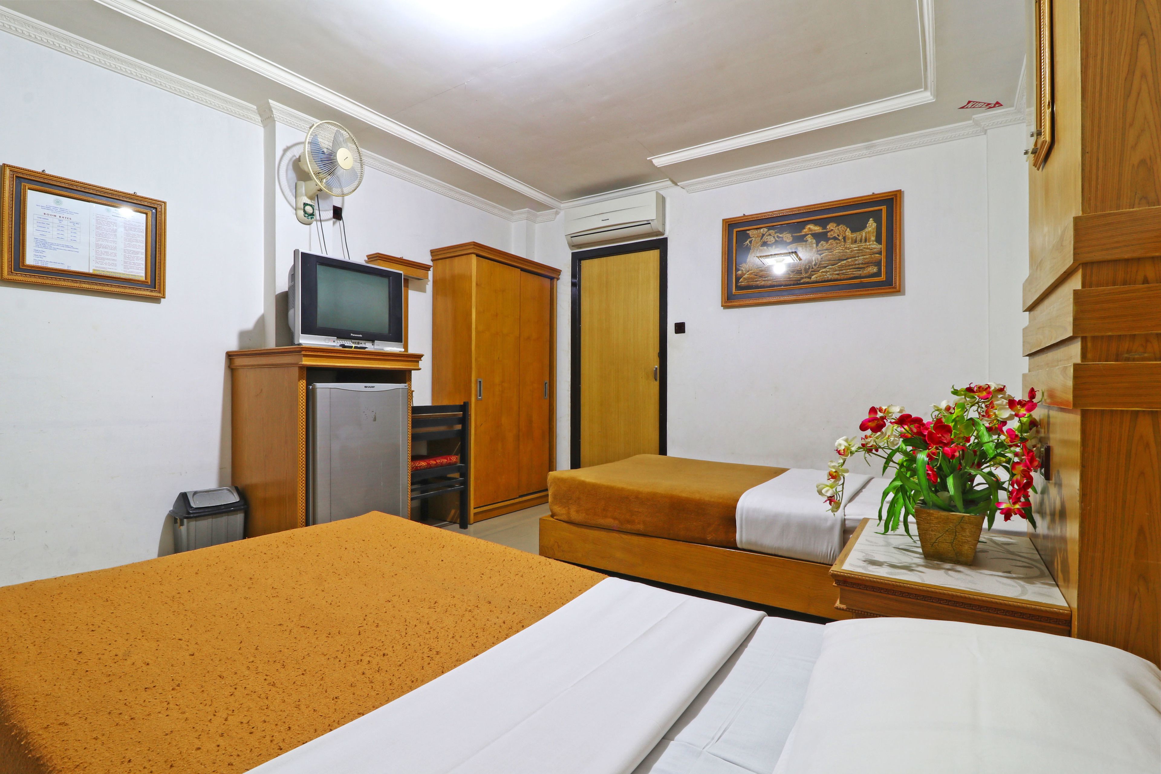 Habitación de hotel con dos camas, un televisor, un escritorio con una planta y un armario de madera.