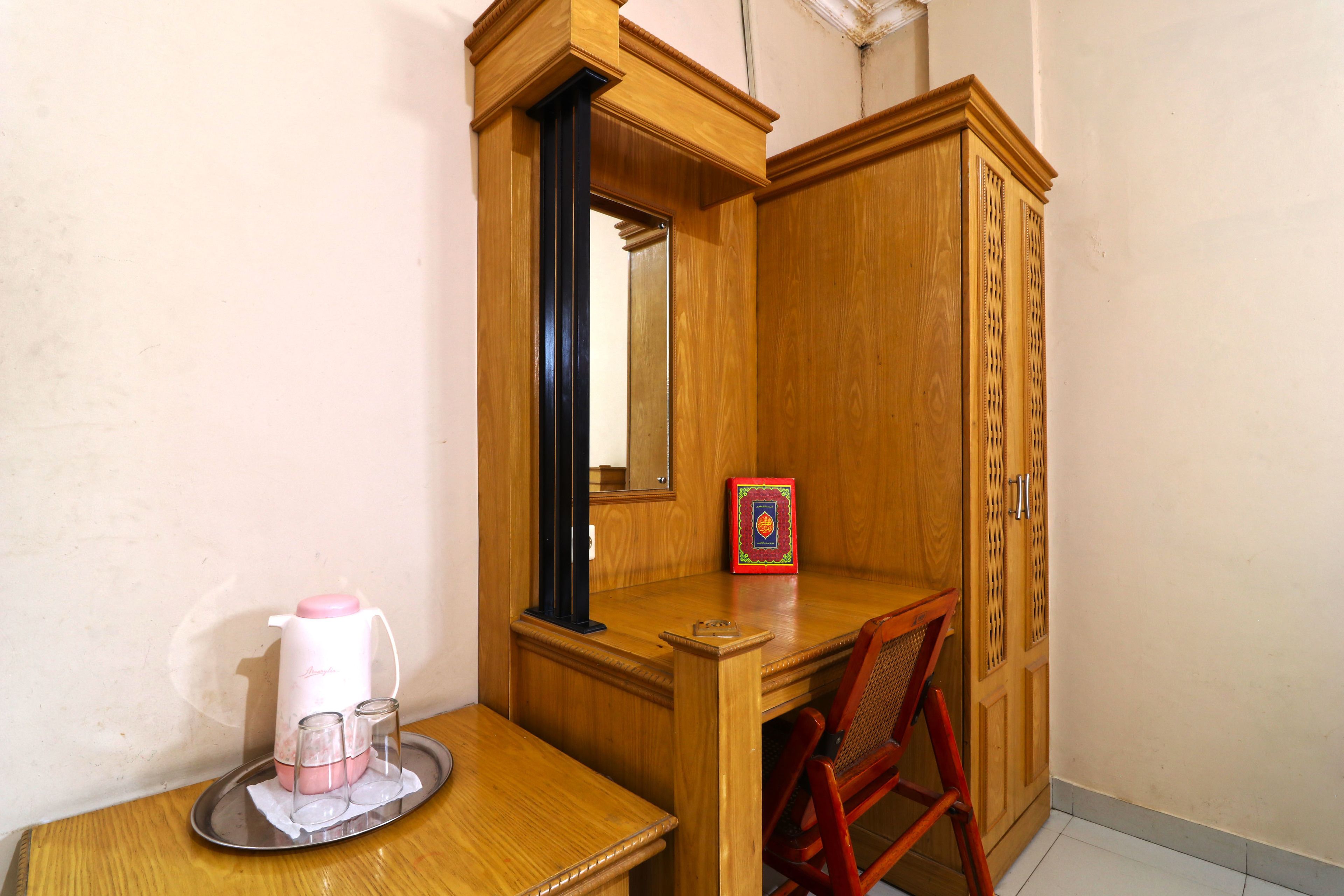 A wooden desk with a mirror, a pink coffee maker, and a red chair.