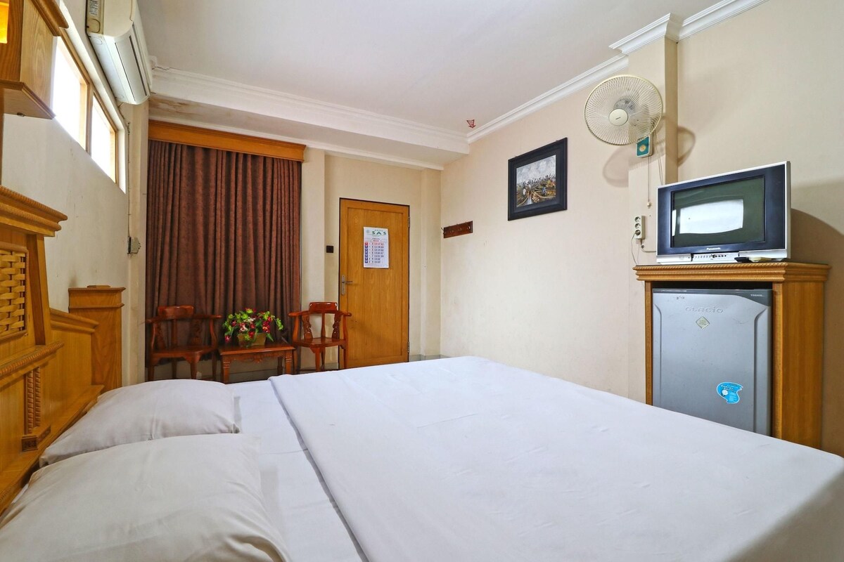 A hotel room with a bed, a desk, a chair, a television, and a refrigerator.