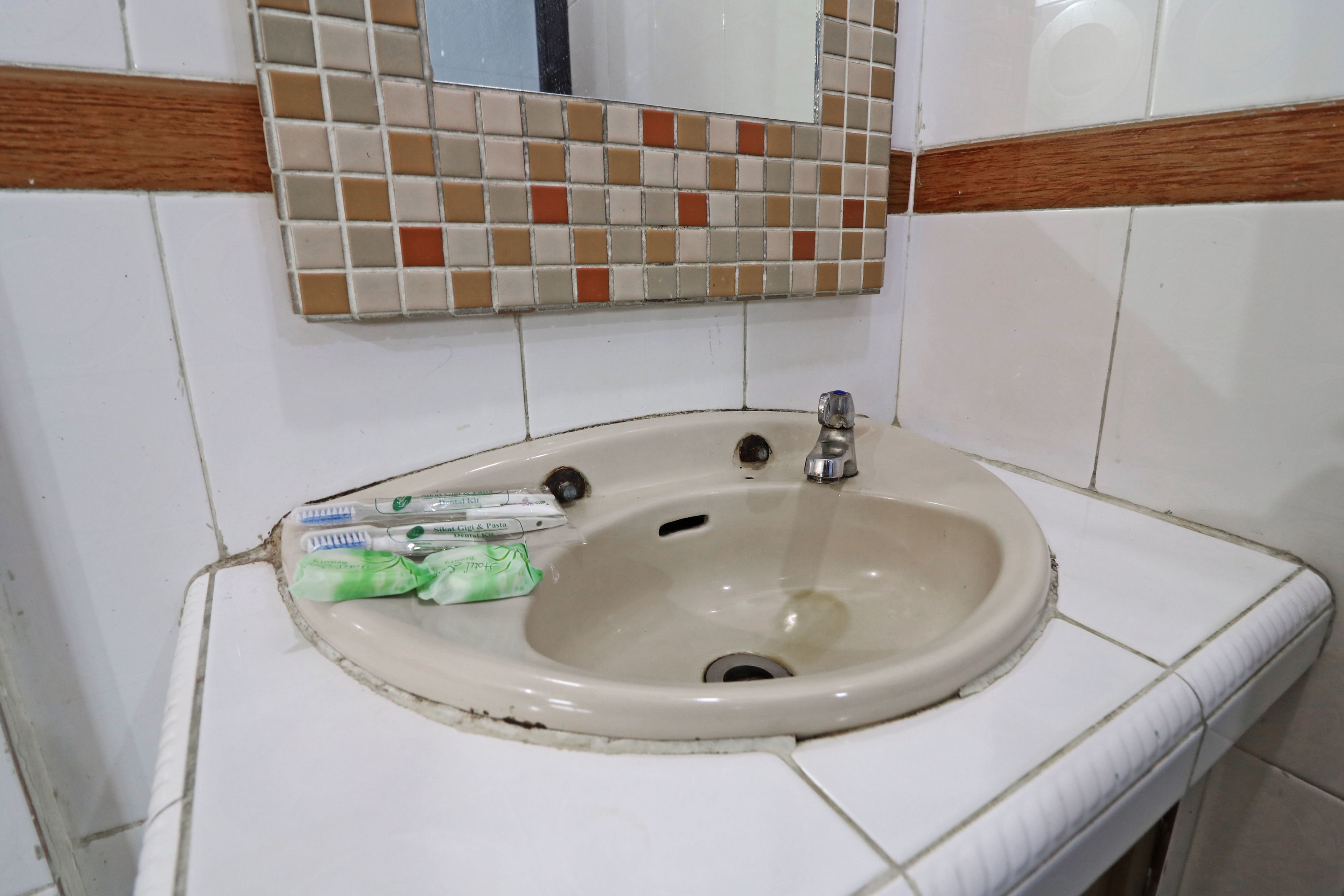 A bathroom sink with a mirror above it, surrounded by white tiles with brown borders.
