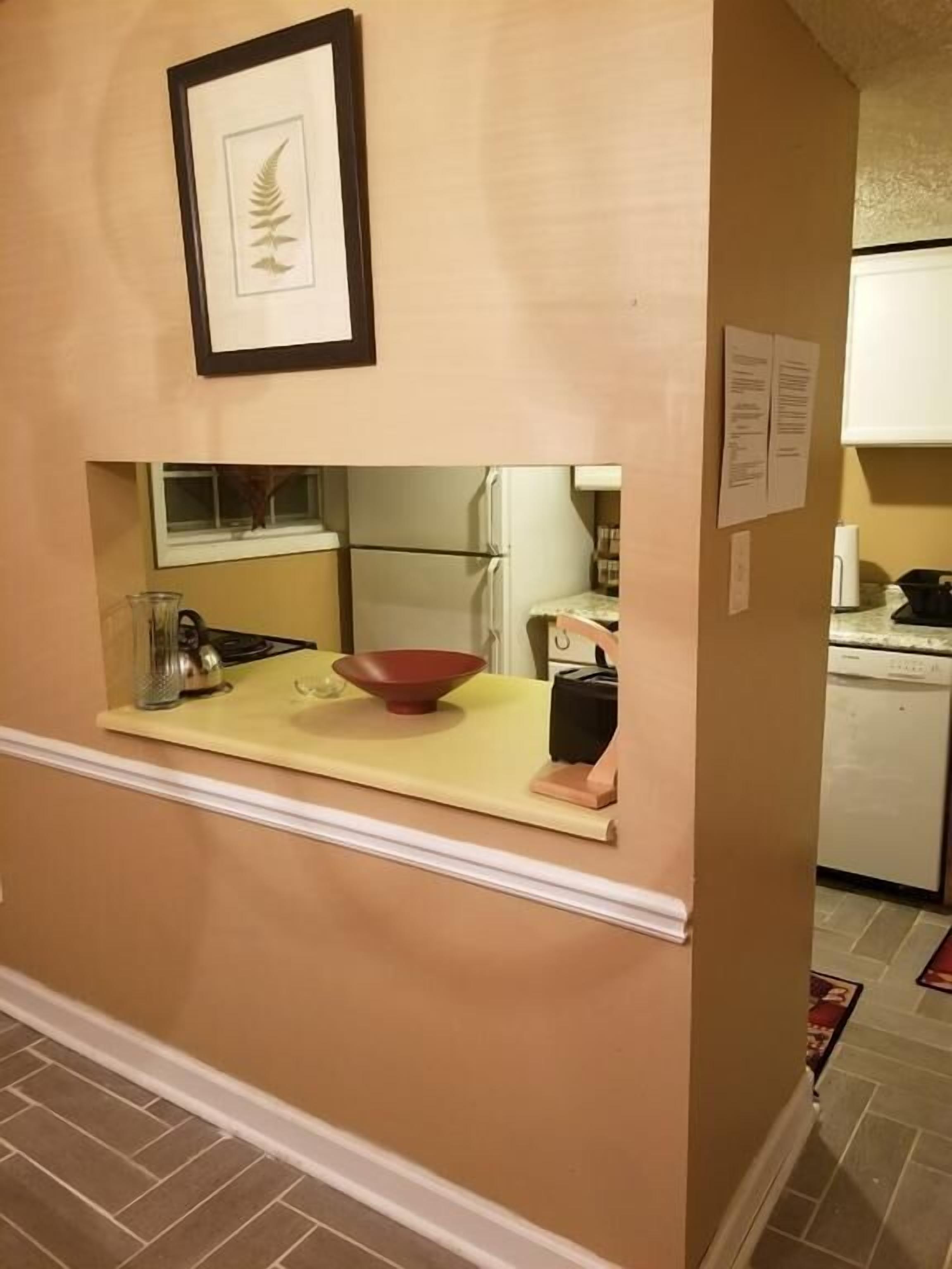 A kitchen with a yellow countertop, a red bowl, a kettle, and a framed leaf decoration on the wall.